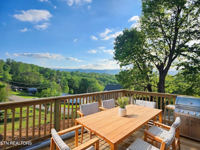 wooden deck with a view of trees, outdoor dining area, and grilling area