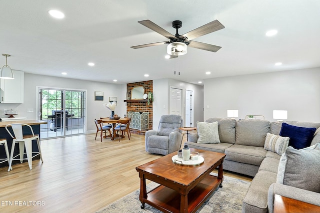 living area featuring recessed lighting, light wood-style flooring, and a brick fireplace