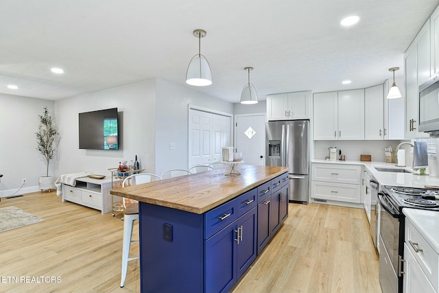 kitchen featuring light wood finished floors, butcher block countertops, a sink, appliances with stainless steel finishes, and blue cabinets