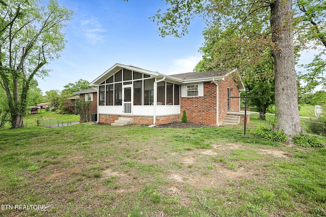 rear view of property featuring fence, a lawn, brick siding, and a sunroom