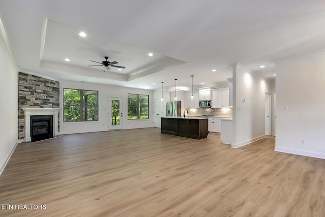 unfurnished living room featuring recessed lighting, light wood-style floors, a raised ceiling, a ceiling fan, and ornamental molding