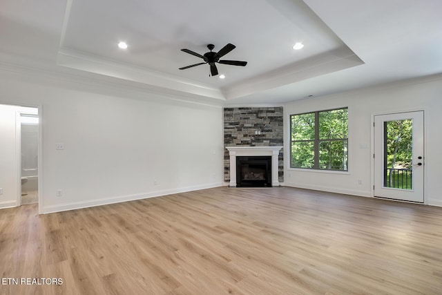 unfurnished living room featuring a tray ceiling, ornamental molding, light wood-type flooring, ceiling fan, and a fireplace