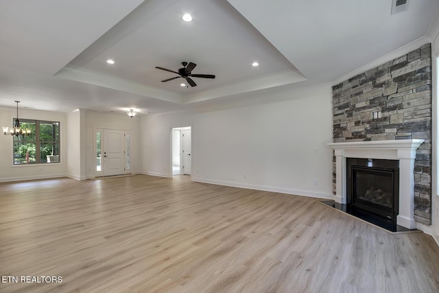 unfurnished living room with a tray ceiling, ornamental molding, ceiling fan, light wood-type flooring, and a stone fireplace