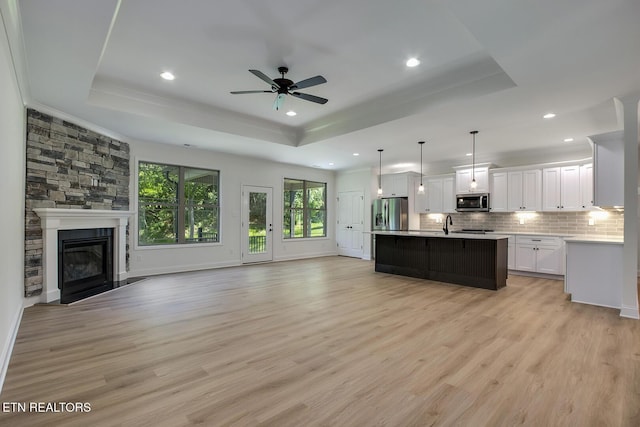 kitchen with open floor plan, a tray ceiling, appliances with stainless steel finishes, light countertops, and backsplash