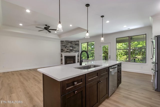 kitchen featuring a sink, appliances with stainless steel finishes, light wood-type flooring, a stone fireplace, and light countertops