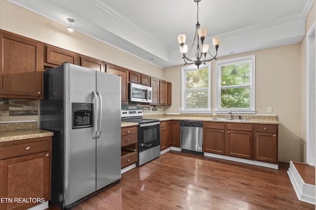 kitchen with a chandelier, brown cabinetry, appliances with stainless steel finishes, a sink, and crown molding