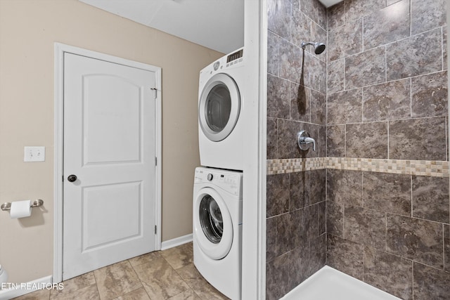 clothes washing area with baseboards, stacked washing maching and dryer, and laundry area