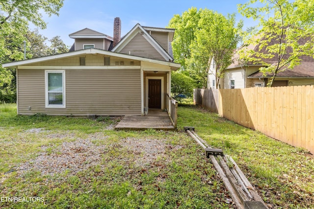 back of house with a chimney, fence, and a lawn
