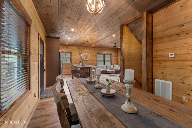 dining area with wooden walls, wood ceiling, an inviting chandelier, light wood-style flooring, and visible vents