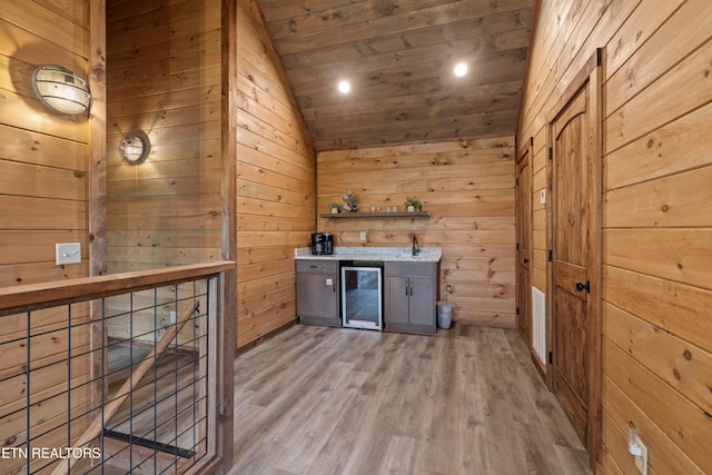 bar with light wood-type flooring, wooden walls, beverage cooler, and vaulted ceiling