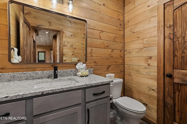 half bath featuring toilet, vanity, and wooden walls