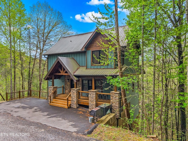 rustic home featuring board and batten siding, a standing seam roof, a porch, stone siding, and metal roof