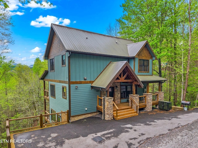 rustic home with covered porch, stone siding, a wooded view, and metal roof