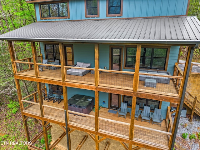 rear view of house with a wooden deck, outdoor dining area, a hot tub, and metal roof
