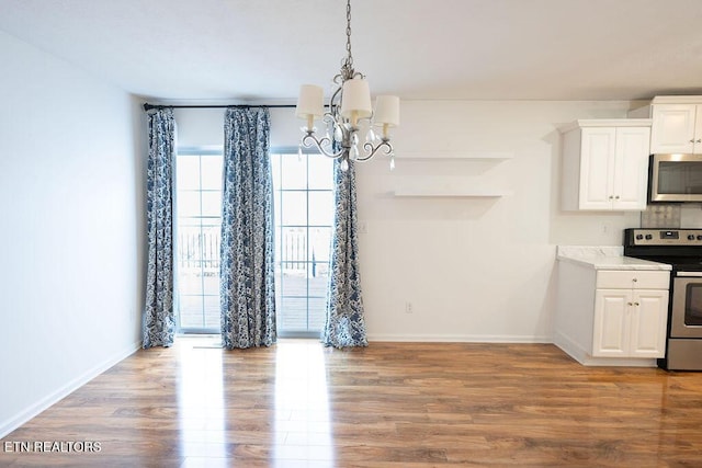 unfurnished dining area with light wood-type flooring, a notable chandelier, and baseboards