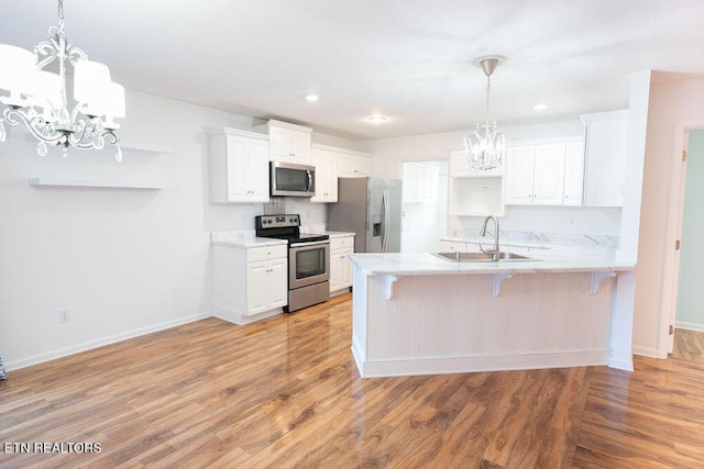 kitchen with stainless steel appliances, a sink, light wood-type flooring, a notable chandelier, and a peninsula