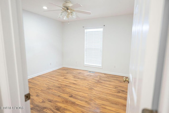 spare room featuring wood finished floors, ceiling fan, visible vents, and baseboards