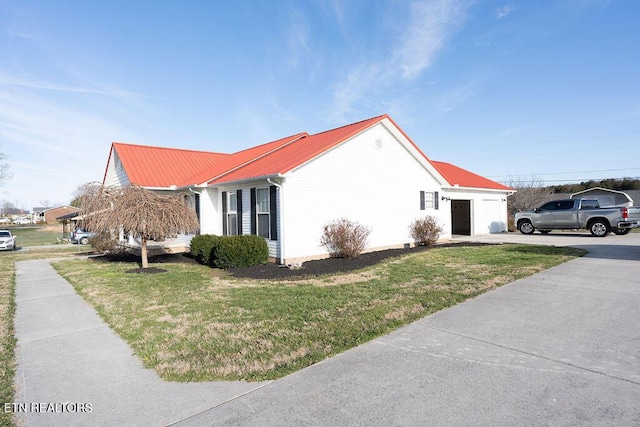 view of property exterior with driveway, metal roof, a lawn, and an attached garage