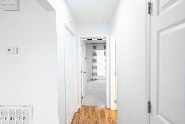 hall featuring baseboards, visible vents, and wood finished floors