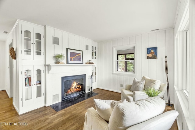 living room featuring a fireplace with flush hearth, wood finished floors, and visible vents