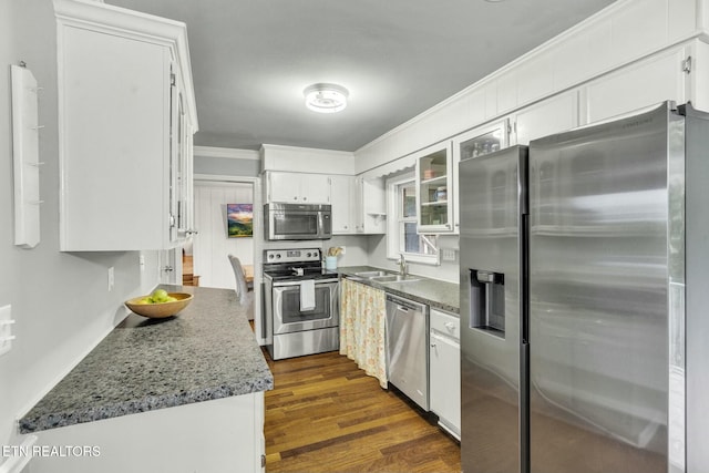 kitchen with appliances with stainless steel finishes, a sink, glass insert cabinets, ornamental molding, and white cabinetry