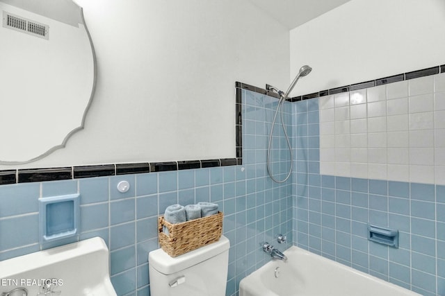 bathroom with visible vents, wainscoting, toilet, tile walls, and shower / washtub combination