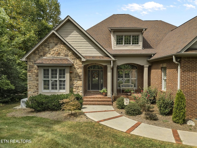 view of front of home featuring a porch, brick siding, roof with shingles, and stone siding