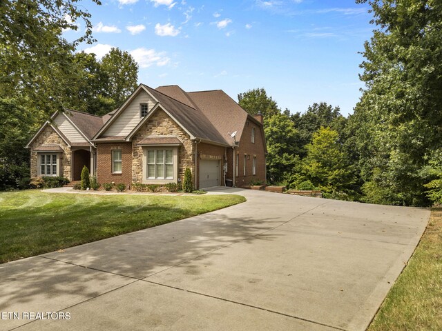 craftsman inspired home featuring driveway, a chimney, a front yard, an attached garage, and stone siding