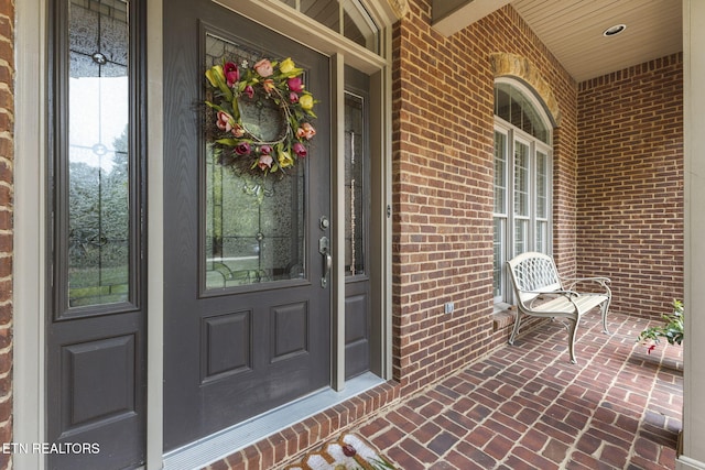 view of exterior entry featuring a porch and brick siding