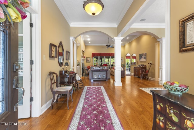 foyer entrance featuring ornate columns, arched walkways, wood finished floors, and ornamental molding
