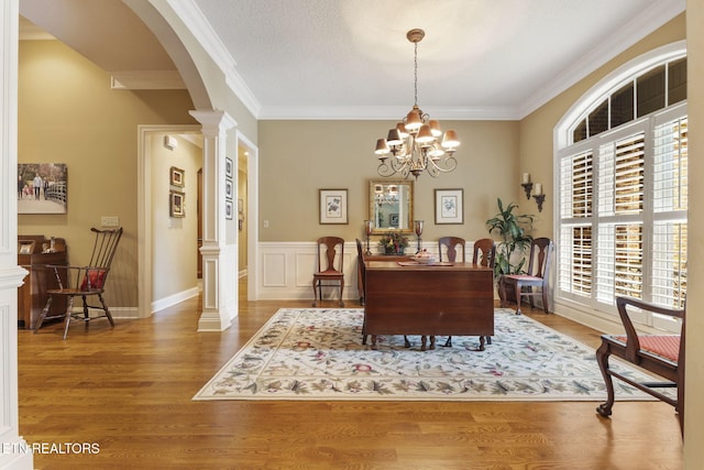 office space with crown molding, arched walkways, decorative columns, and wood finished floors