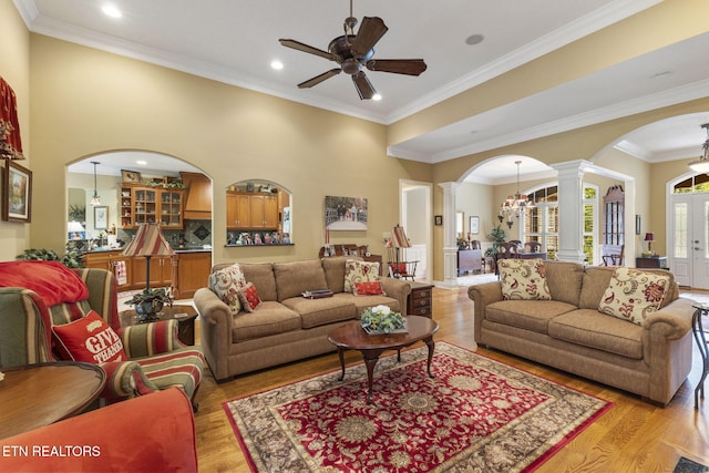 living area with crown molding, ceiling fan, ornate columns, light wood-type flooring, and arched walkways