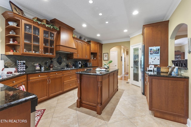 kitchen featuring arched walkways, tasteful backsplash, open shelves, custom exhaust hood, and ornamental molding