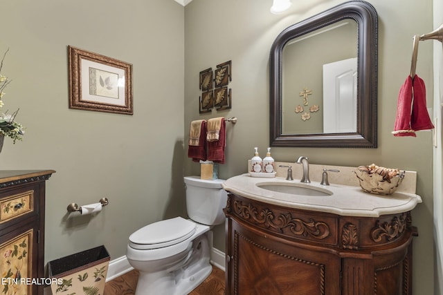 half bath with toilet, baseboards, wood finished floors, and vanity