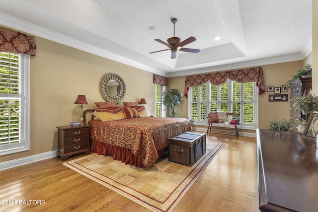 bedroom with baseboards, a textured ceiling, light wood-style flooring, and a tray ceiling