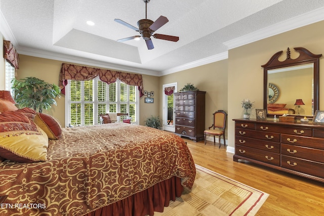 bedroom with a ceiling fan, a textured ceiling, light wood-type flooring, a raised ceiling, and ornamental molding