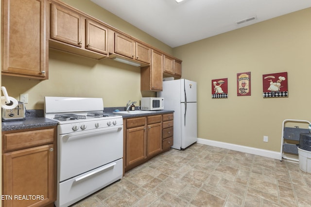 kitchen with dark countertops, white appliances, baseboards, stone finish floor, and a sink