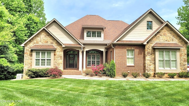 craftsman inspired home with roof with shingles, stone siding, brick siding, and a front yard