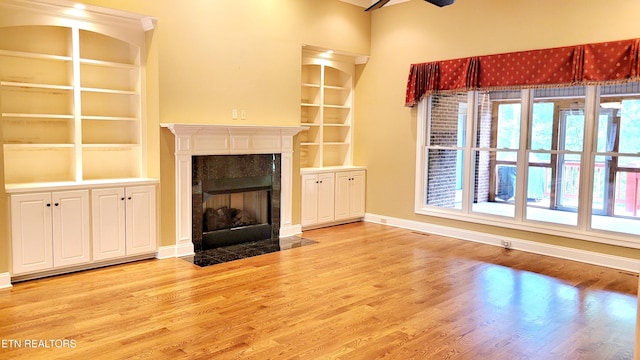 unfurnished living room with ceiling fan, built in features, light wood-type flooring, baseboards, and a premium fireplace
