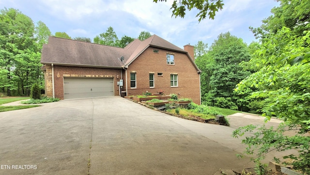 view of front of home featuring brick siding, a garage, driveway, and a chimney