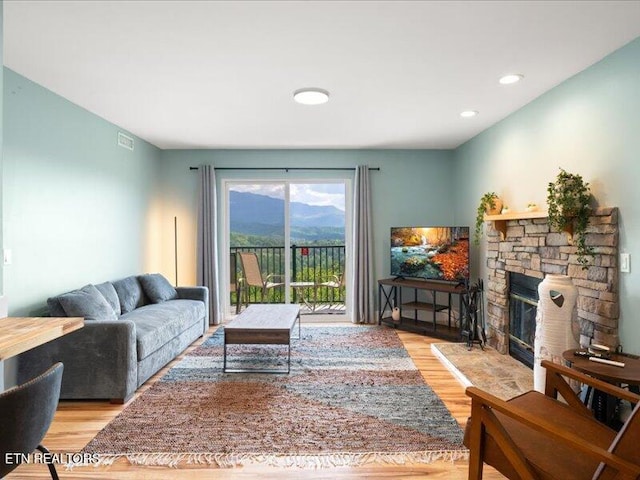 living room with recessed lighting, visible vents, a stone fireplace, and wood finished floors