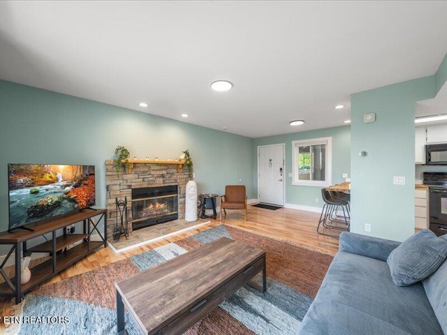 living room with recessed lighting, baseboards, a stone fireplace, and wood finished floors
