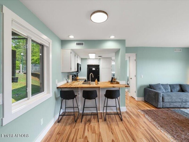 kitchen with visible vents, light wood-type flooring, white cabinets, a peninsula, and butcher block countertops