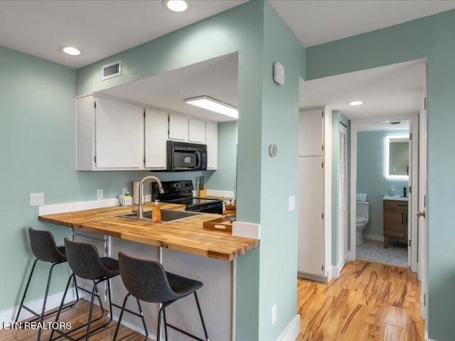 kitchen featuring visible vents, butcher block counters, light wood-style floors, white cabinetry, and black appliances