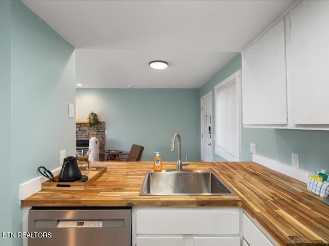 kitchen featuring stainless steel dishwasher, white cabinetry, butcher block counters, and a sink
