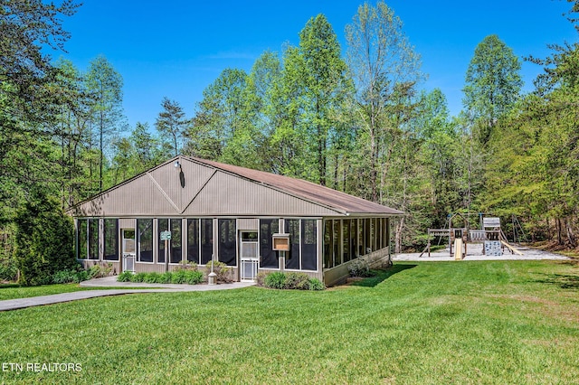 rear view of property with a sunroom, a playground, and a lawn