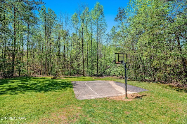view of basketball court with a yard, a wooded view, and basketball court