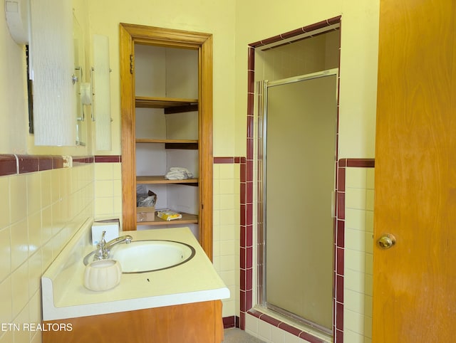 bathroom with vanity, a shower stall, wainscoting, and tile walls