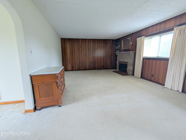 unfurnished living room featuring a brick fireplace, wood walls, light carpet, and baseboards