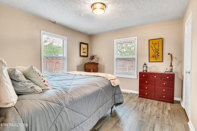 bedroom with baseboards, wood finished floors, a textured ceiling, and multiple windows